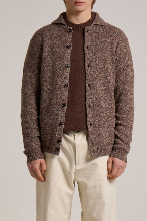 Person wearing a brown textured cardigan over a brown sweater with beige pants on a plain background